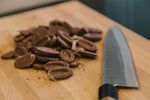 Cutting board with cocoa beans cut in half and a knife on it