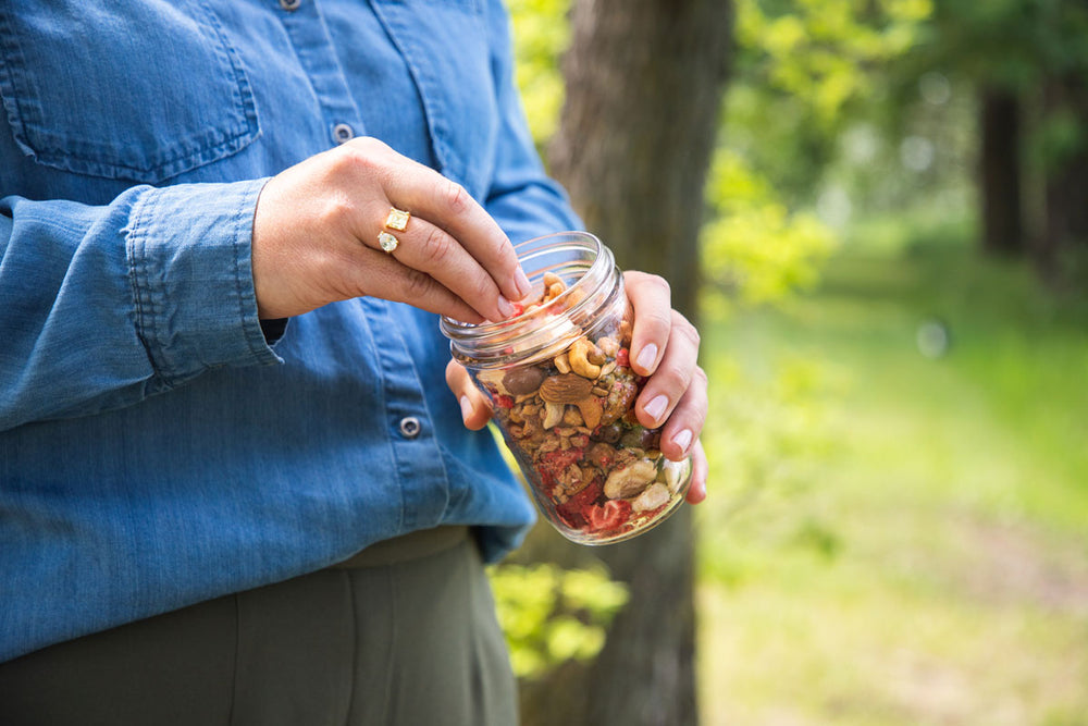 hand picking trail mix out of a mason jar while in the forest