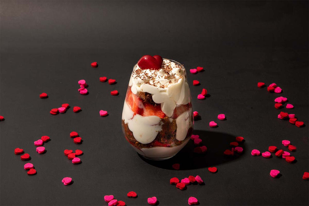 heart shaped confetti surrounding a parfait with a cherry on top on a black background