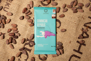 A teal chocolate bar wrapper, picturing an illustrated depiction of the country Dominican Republic, sits on a burlap sack among scattered cocoa beans.