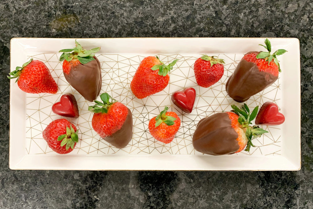 While plate with twelve chocolate covered strawberries on a dark countertop