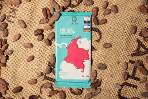A teal chocolate bar wrapper, picturing an illustrated depiction of the country Colombia, sits on a burlap sack among scattered cocoa beans.