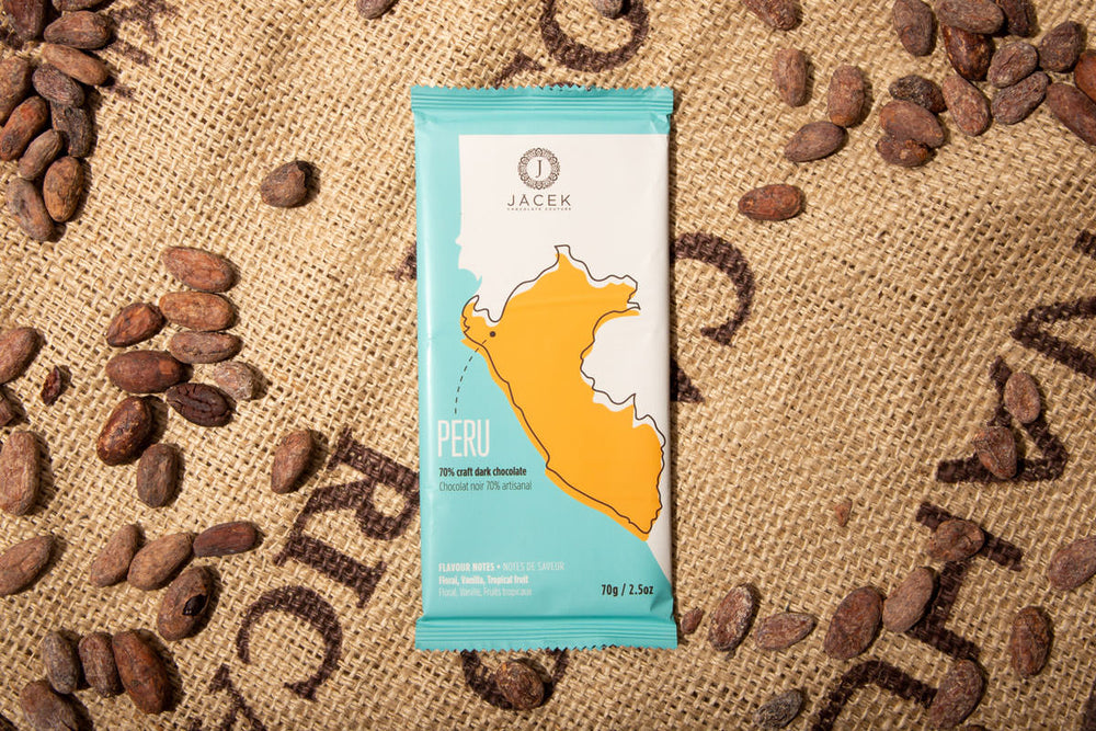 A teal chocolate bar wrapper, picturing an illustrated depiction of the country Peru, sits on a burlap sack among scattered cocoa beans.
